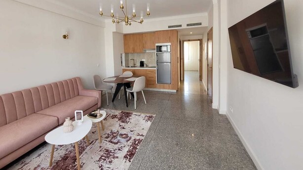 Un salon moderne avec un canapé rose, une table à manger avec des chaises, et une cuisine en arrière-plan.