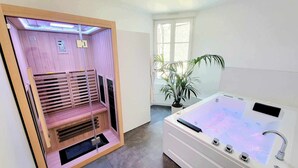 Un sauna doté d’un panneau de commande et d’un fauteuil de massage, une grande fenêtre offrant une vue dégagée et une baignoire blanche avec un panneau de commande.