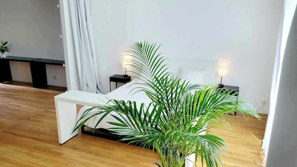 A modern bedroom with a white bed, bedside tables, a bench, and potted plants. - SPA Aparthotel: Jacuzzi, sauna, terrace, balcony, city center, Place Drouet D'Erlon (Reims)