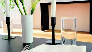 Une table à manger élégamment dressée, avec une assiette blanche, une serviette pliée, un verre d’eau et deux bougies dans des bougeoirs noirs.