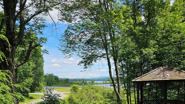 A gazebo in a lush green area with a view of a lake and distant mountains. - 2-bedroom Lakeview house near Tupper Lake with AC, WiFi, Deck, Gazebo, Firepit (Piercefield)