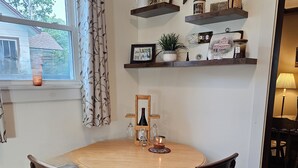 A dining area with a round wooden table, two upholstered chairs, and a window with a view of a house. - 2-bedroom Lakeview house near Tupper Lake with AC, WiFi, Deck, Gazebo, Firepit (Piercefield)