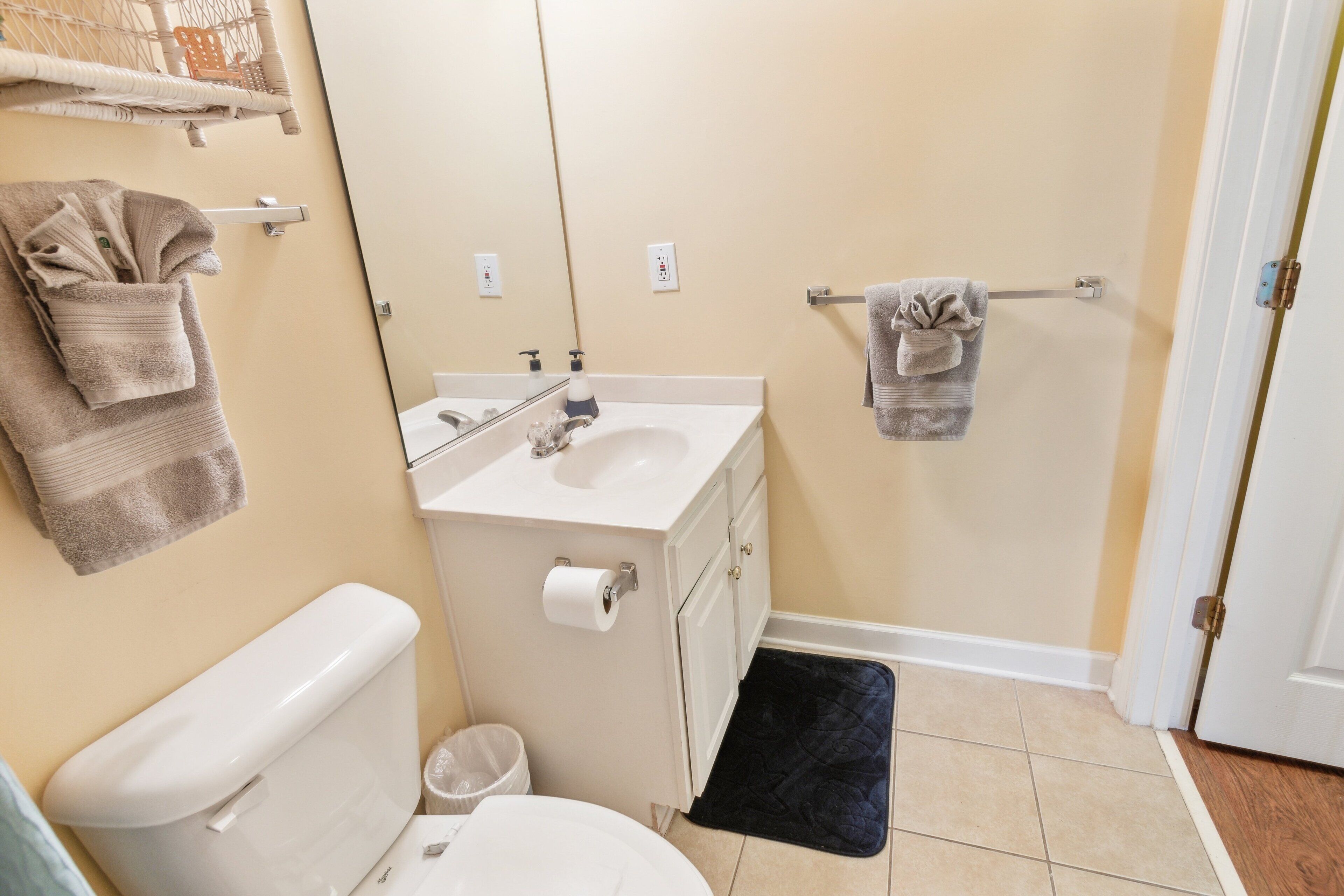 A bathroom with a toilet, sink, mirror, towel rack, and a black mat.