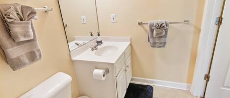 A bathroom with a toilet, sink, mirror, towel rack, and a black mat.