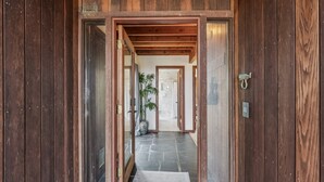 A wooden door leading to a hallway with a stone floor and a potted plant. - Beach Gem Scenic Views & BBQ Yard (Manchester)