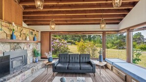 Ein modernes Wohnzimmer mit Kamin aus Stein, einem grauen Sofa und einem großen Fenster mit Blick auf einen Garten.