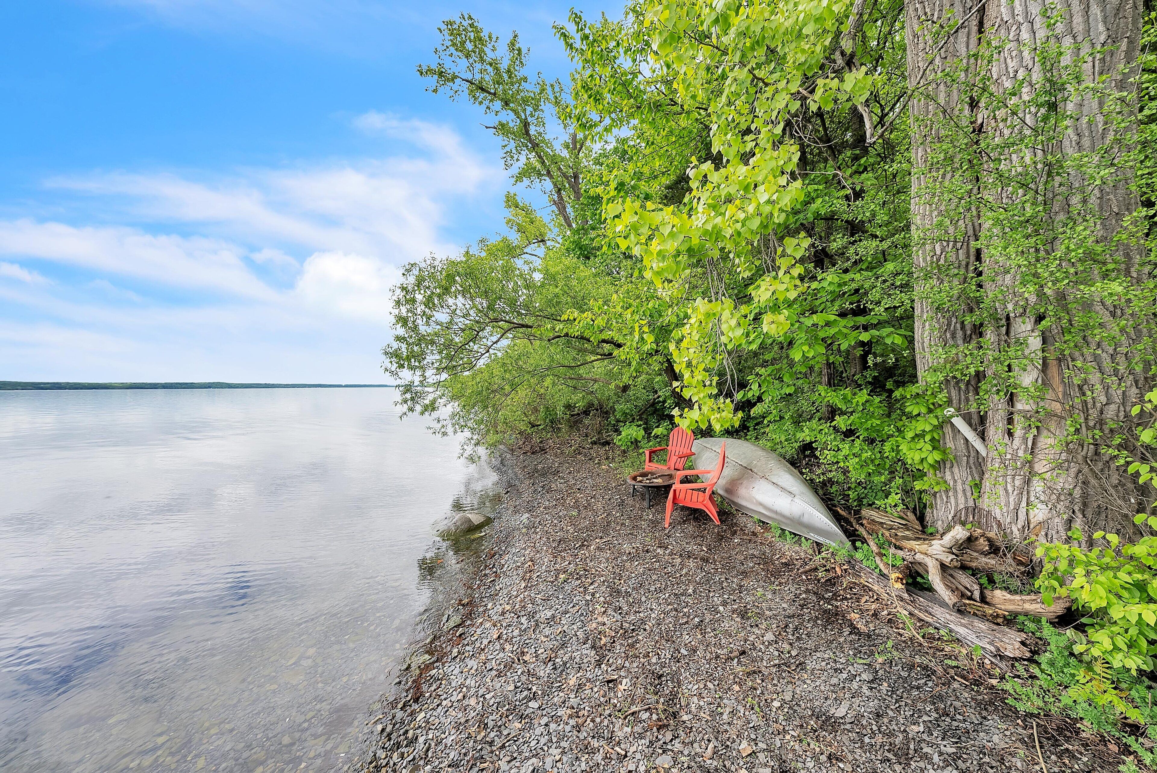A serene lakeside setting with a row of red chairs and a canoe by a tree-lined shore.