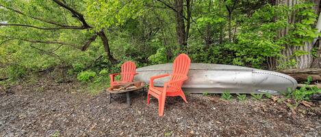 Una canoa y dos sillas Adirondack en un área boscosa.