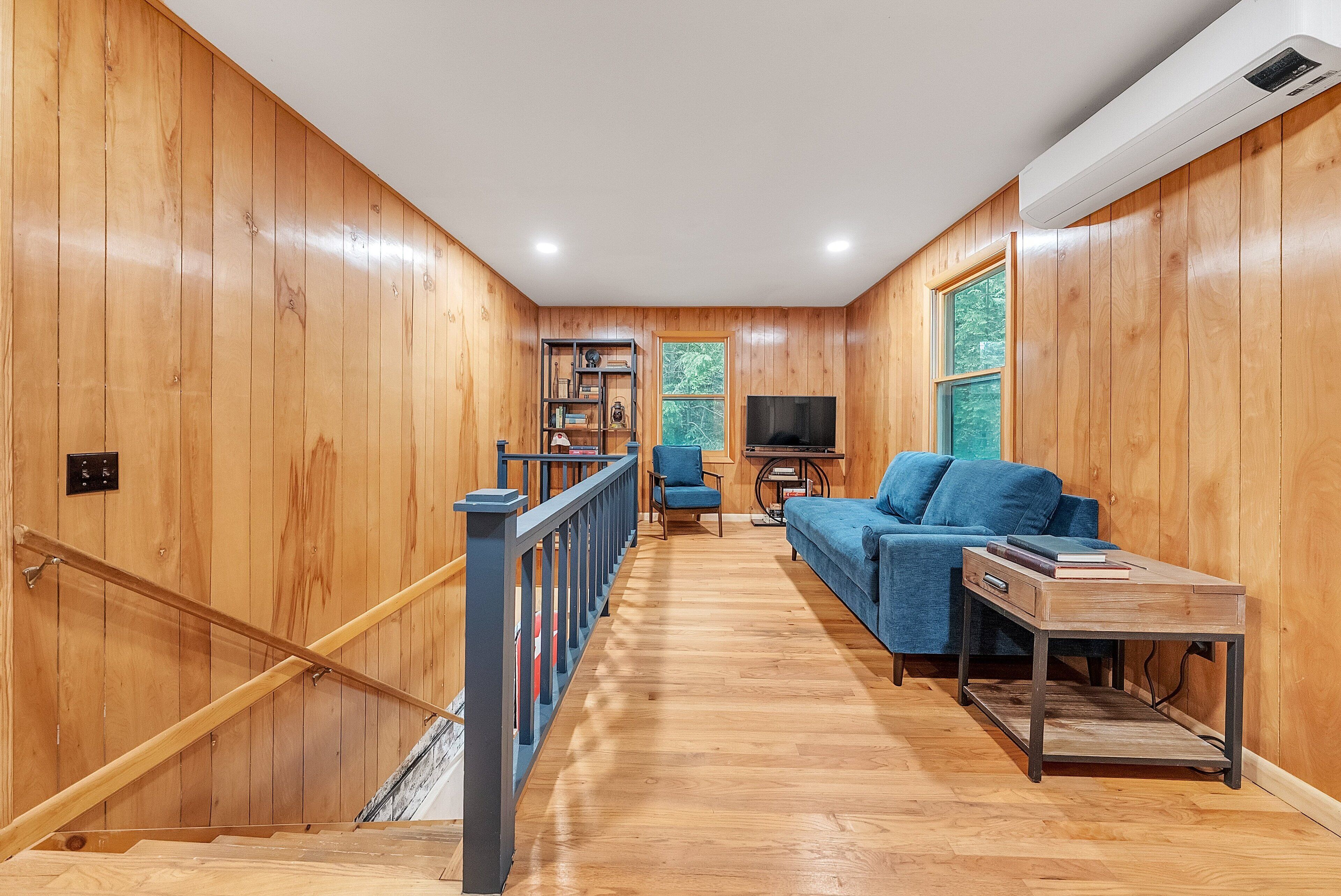 A wooden-paneled room with a staircase, a blue sofa, a TV, and a bookshelf.