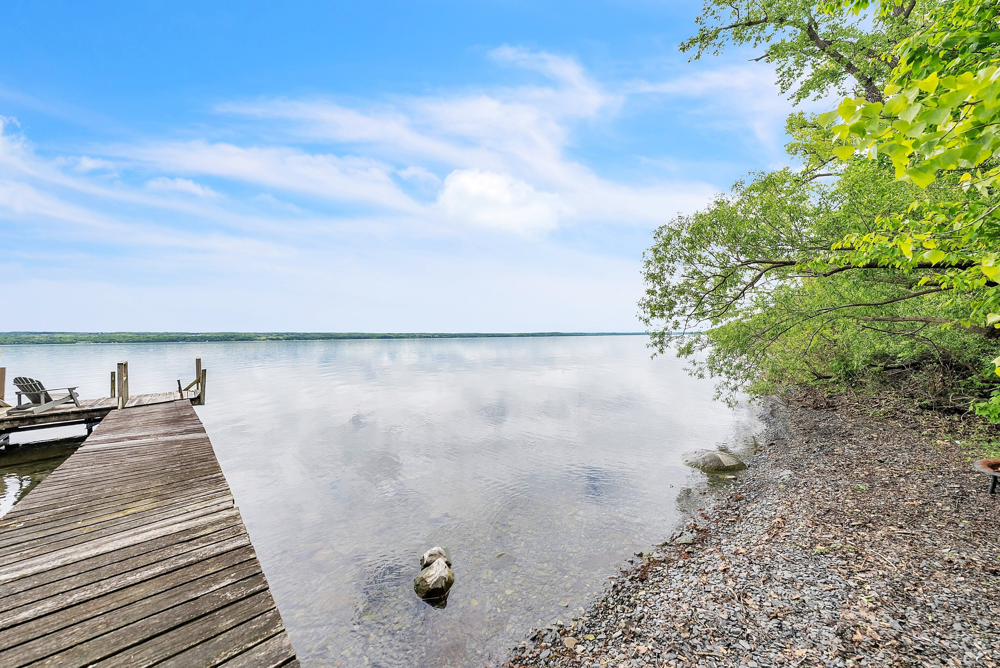 A wooden dock extending into calm water, surrounded by pebbles and greenery.
