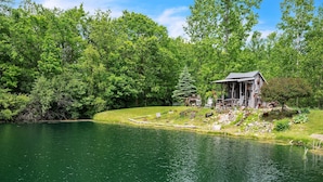 A lakeside cabin with a deck, surrounded by dense forest. - Lakeside Retreat With Hot Tub & Game Room 3 Bedroom Home (Elkhart)