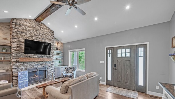 A living room with a stone fireplace, a flat-screen TV, a sofa, and a ceiling fan. - Lakeside Retreat With Hot Tub & Game Room 3 Bedroom Home (Elkhart)