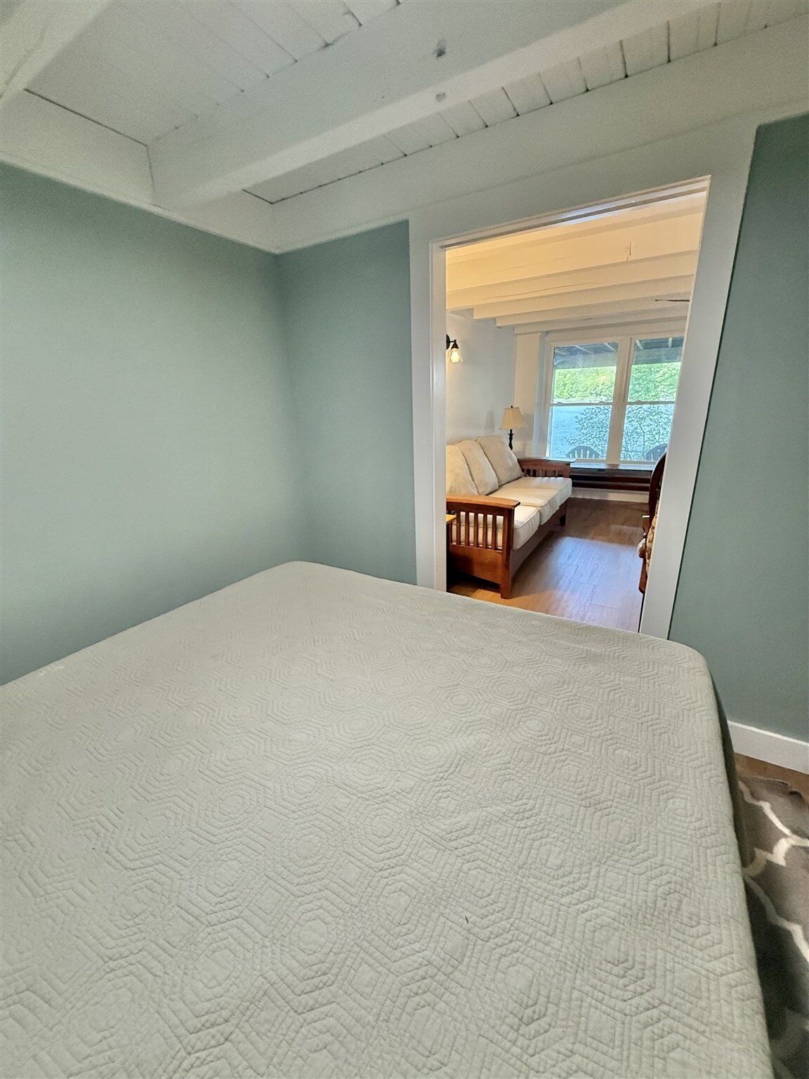 Une chambre avec un grand lit, un banc en bois et une vue sur un espace extérieur, visible à travers une porte.