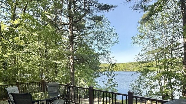 Une terrasse en bois, agréée de mobilier d’extérieur, qui offre une vue sur un lac entouré d’arbres.