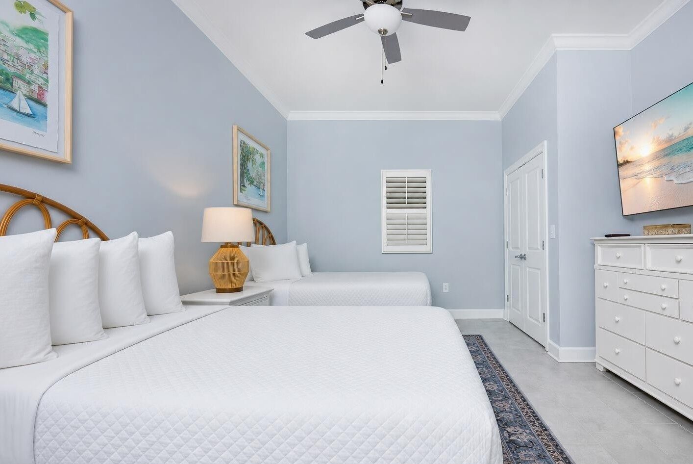 Une chambre avec deux lits, un ventilateur de plafond, une télévision, une commode et une fenêtre avec des stores.