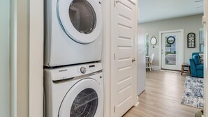 A laundry room with two stacked front-loading washing machines, a white door, and a hallway leading to a dining area. - Nauta Mirage 2 Bedroom Home (Rockport)