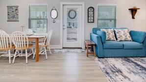 A living room with a blue sofa, white chairs, a wooden dining table, and a door with a wreath. - Nauta Mirage 2 Bedroom Home (Rockport)