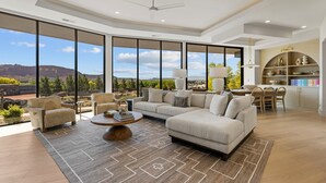 Un vaste salon doté d’une grande fenêtre offrant une vue sur les montagnes, d’un ventilateur de plafond et d’un coin repas avec une cuisine en arrière-plan.