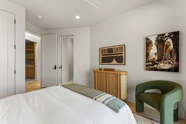 Un dormitorio con una cama, una silla verde, un armario de madera y un cuadro en la pared.