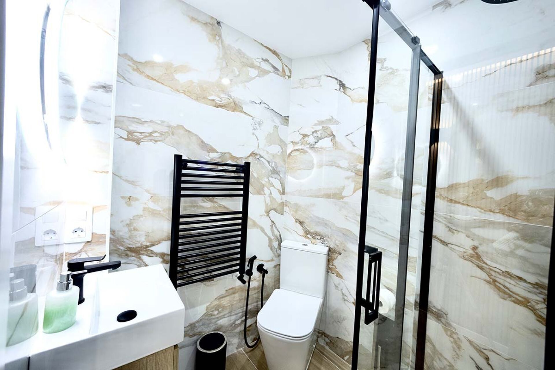 Une salle de bain avec un mur en marbre, un porte-serviettes noir, des toilettes blanches et une cabine de douche en verre.