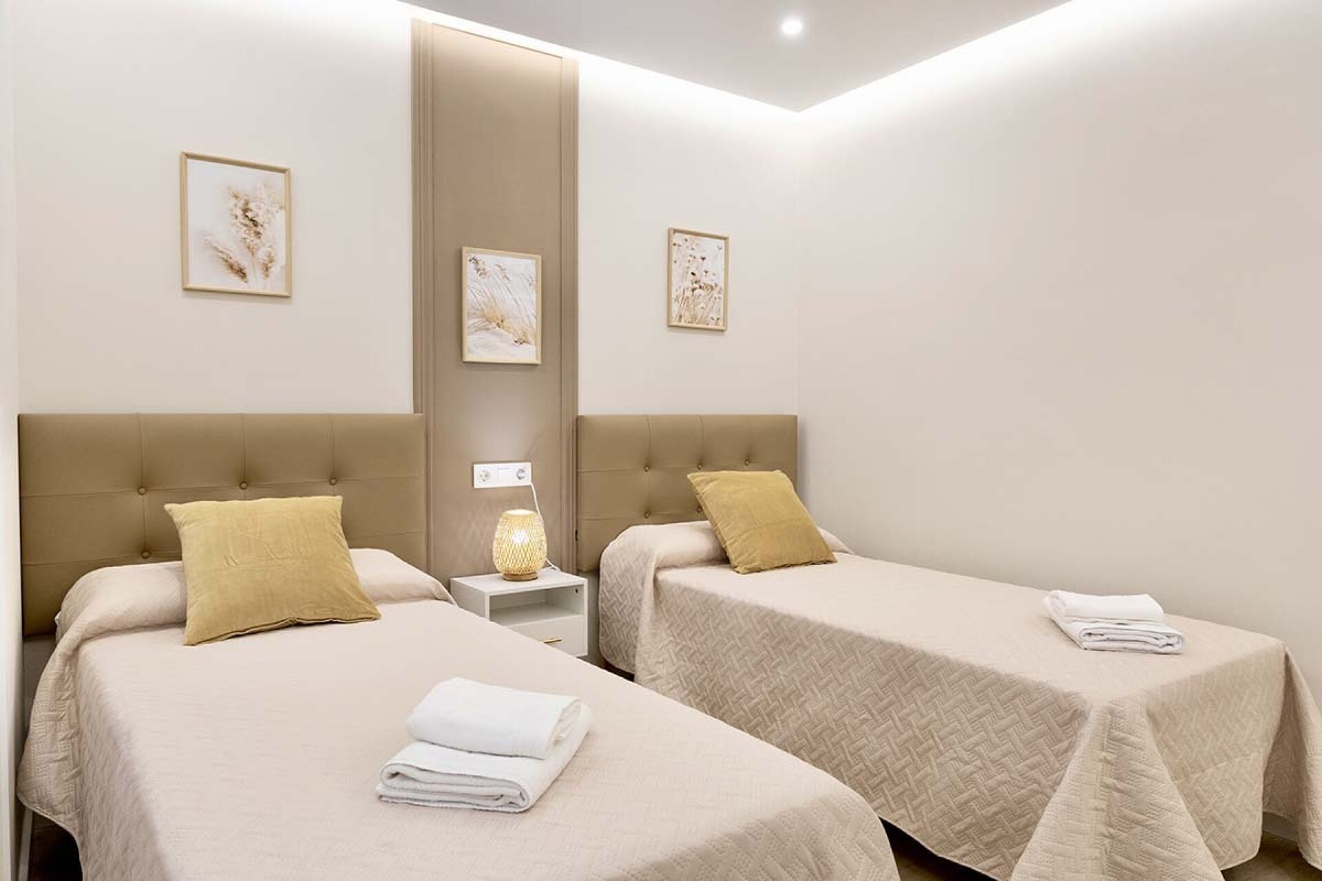 Habitación de hotel con dos camas, cada una con cabecera, mesita de noche y lámpara.