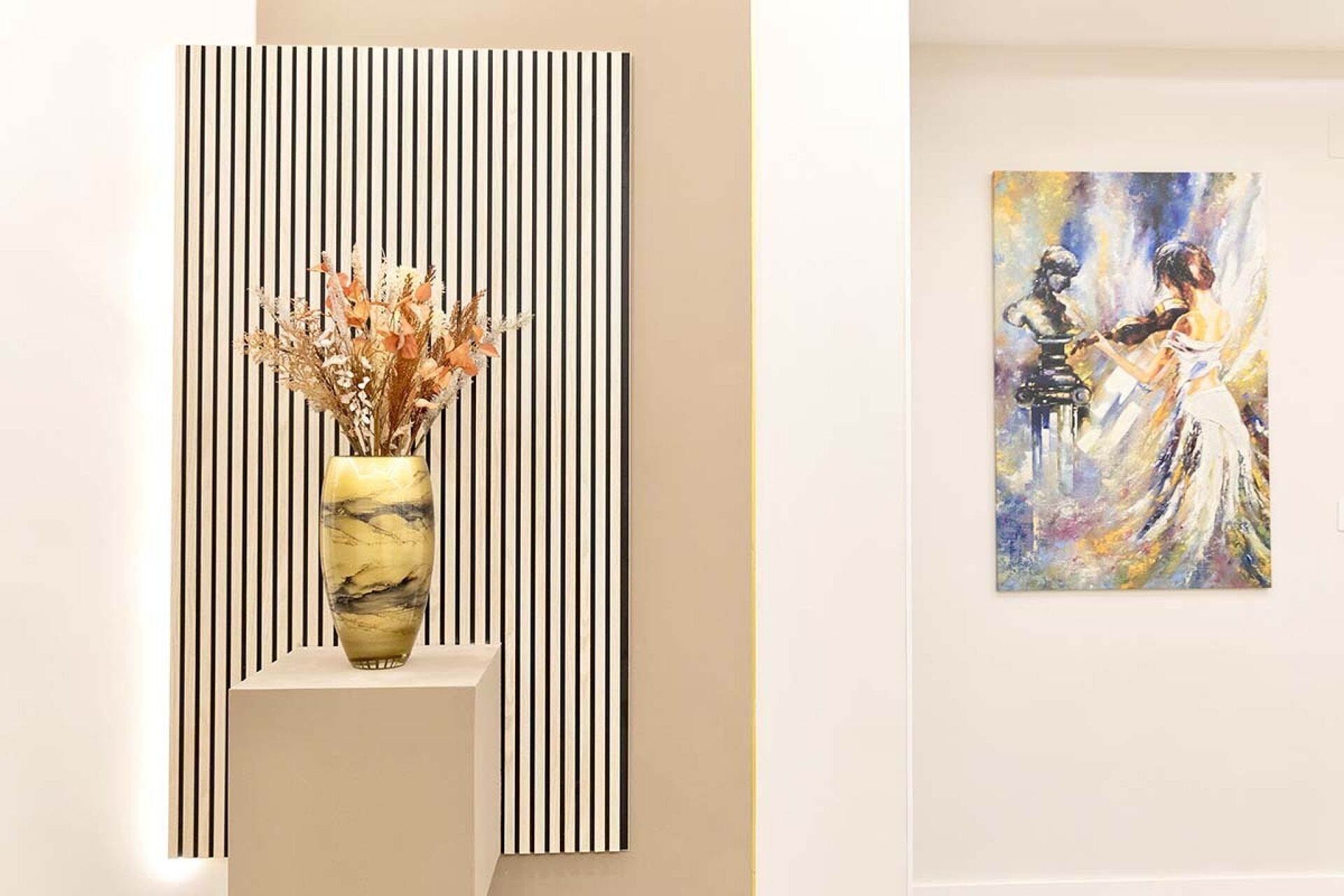 Un interior moderno con una pared a rayas, un jarrón con flores secas y un cuadro con la imagen de dos personas.