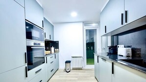A narrow kitchen with white cabinets, a built-in oven, and a window overlooking a green outdoor area.