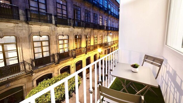 A balcony with a table and chairs, overlooking a building with multiple windows and balconies.