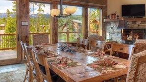 A spacious dining area with a large wooden table, multiple chairs, and a stone fireplace. - 5BR Ski-In/Ski-Out Cabin, Hot Tub, Fireplace & Mountain Views – Big Sky, MT (Big Sky)
