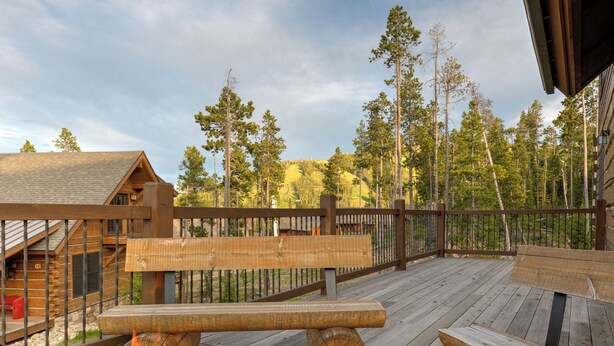 A wooden deck with a fire pit, benches, and a wooden fence overlooking a forested area. - 5BR Ski-In/Ski-Out Cabin, Hot Tub, Fireplace & Mountain Views – Big Sky, MT (Big Sky)