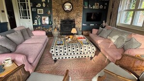 A cozy living room with a brick fireplace, two sofas, a coffee table, and a bookshelf filled with books and decorative items. - Stunning Rectory, 15 guests in Surrey (South Nutfield)