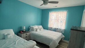 Une chambre avec deux lits, un ventilateur de plafond, une table de chevet avec une lampe et une fenêtre avec des rideaux.