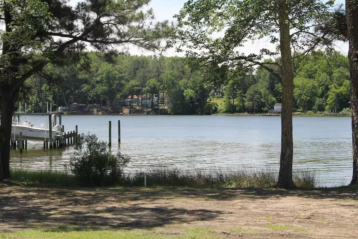 Un lac avec un quai et des bateaux, entouré d’arbres et avec un bâtiment visible au loin.