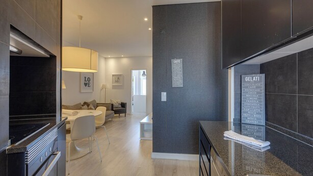 Una cocina moderna con horno empotrado, una zona de comedor con mesa y sillas blancas, y una pared de acento gris con un cartel de menú.