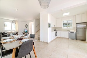 A modern kitchen with white cabinets, stainless steel appliances, and a dining area with a table set for four. - Green Bay Villa 14 in Protaras (Paralimni)