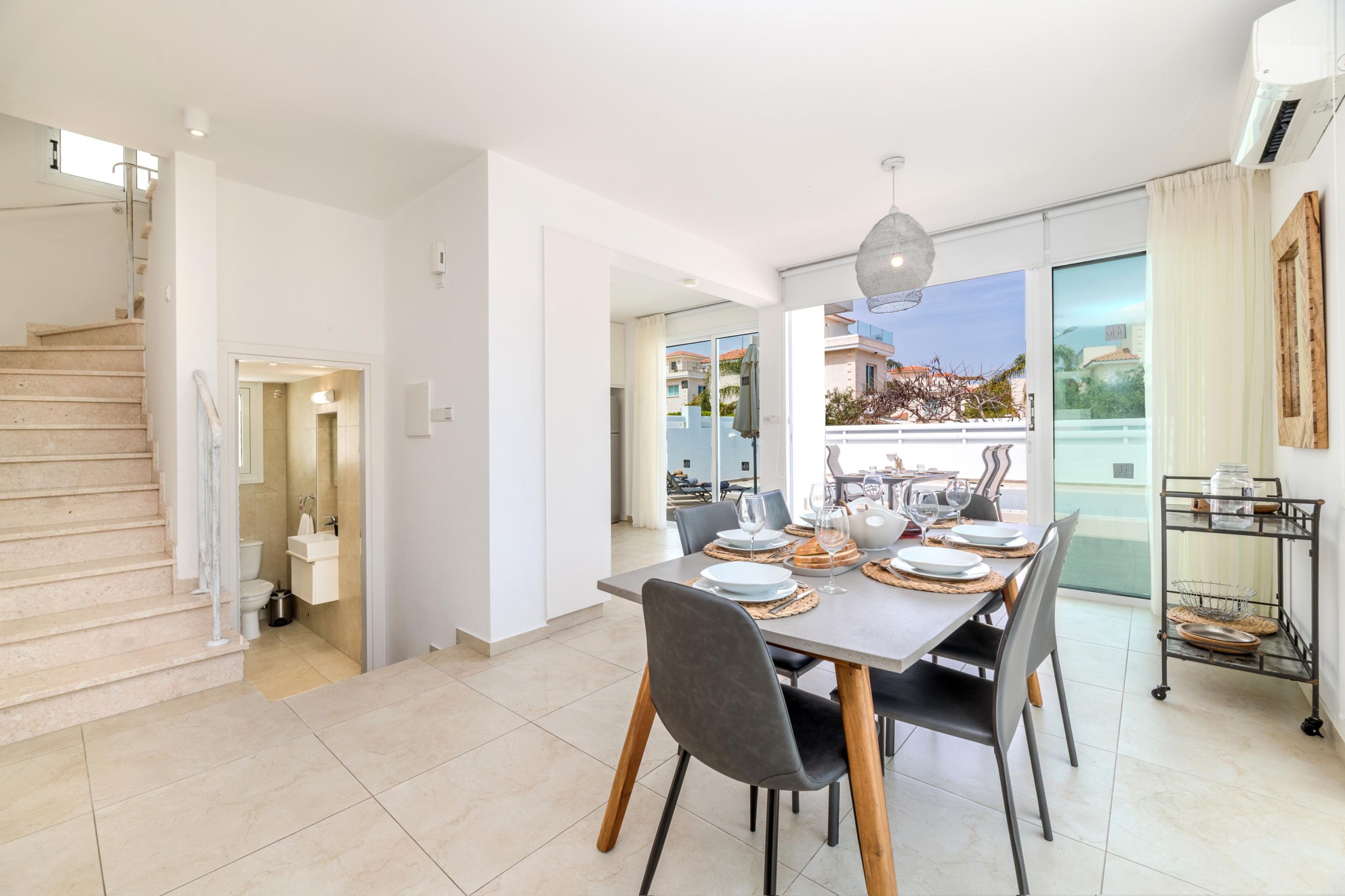 A modern dining area with a large table set for six, a staircase, and a view of the outside.
