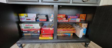Un meuble en bois doté de deux tiroirs et d’une étagère, contenant divers jeux de société.