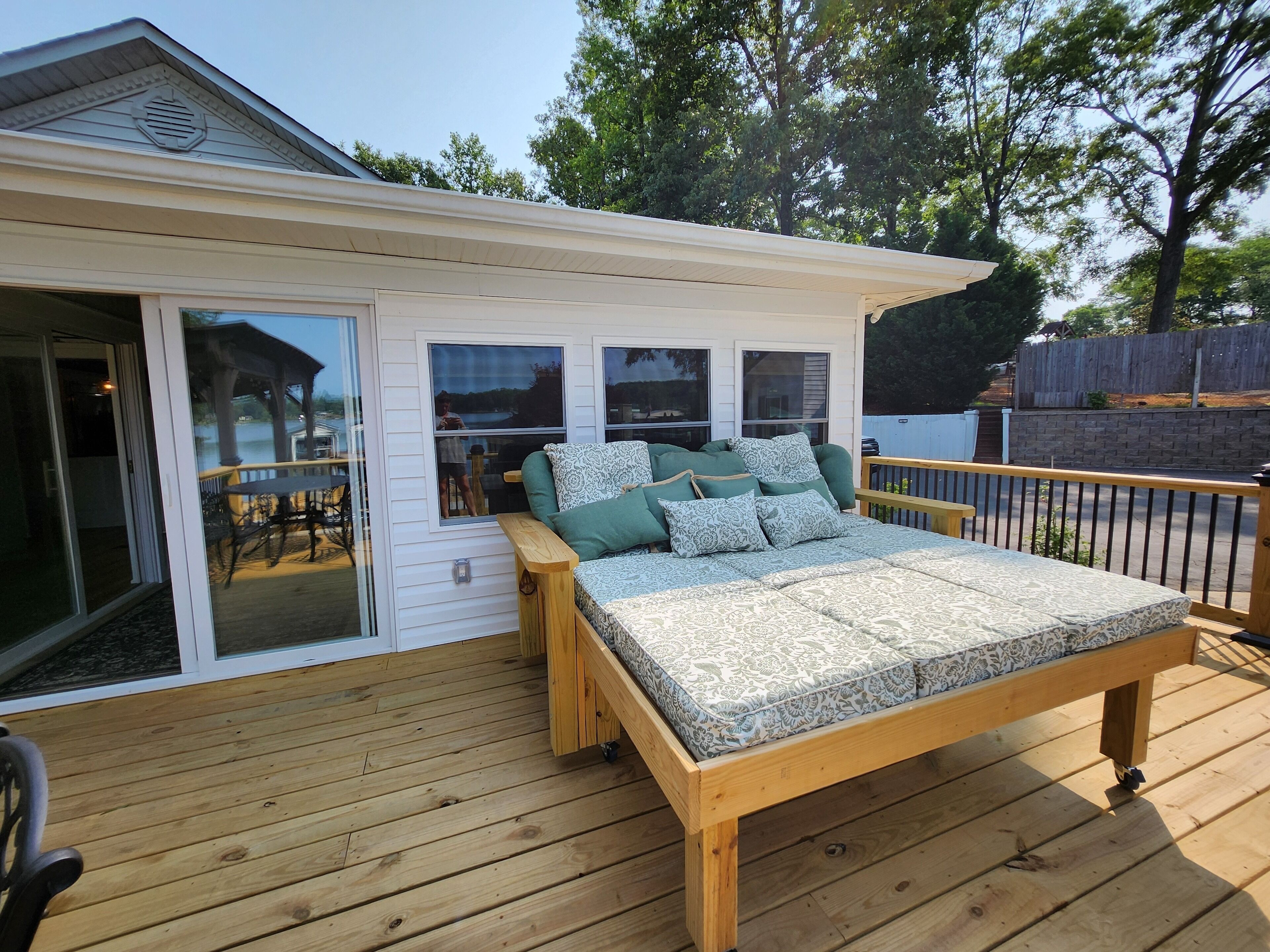Un dormitorio con una cama de madera, un ventanal corredero y vistas a un patio con mobiliario exterior.