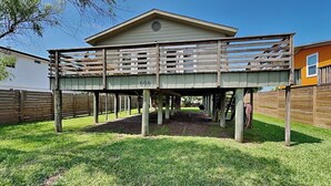 A wooden deck structure with a number 606, supported by posts, in a grassy yard with a fence and a building in the background.