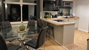 A modern kitchen with a central island, black chairs around a glass table, and a large window with curtains. - Home from Home, only 5 minutes drive from Historical Durham center. (Durham)
