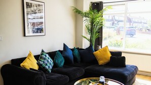 A living room with a black sofa, yellow and blue patterned pillows, a glass coffee table, and a large window with a view of a street. - Home from Home, only 5 minutes drive from Historical Durham center. (Durham)