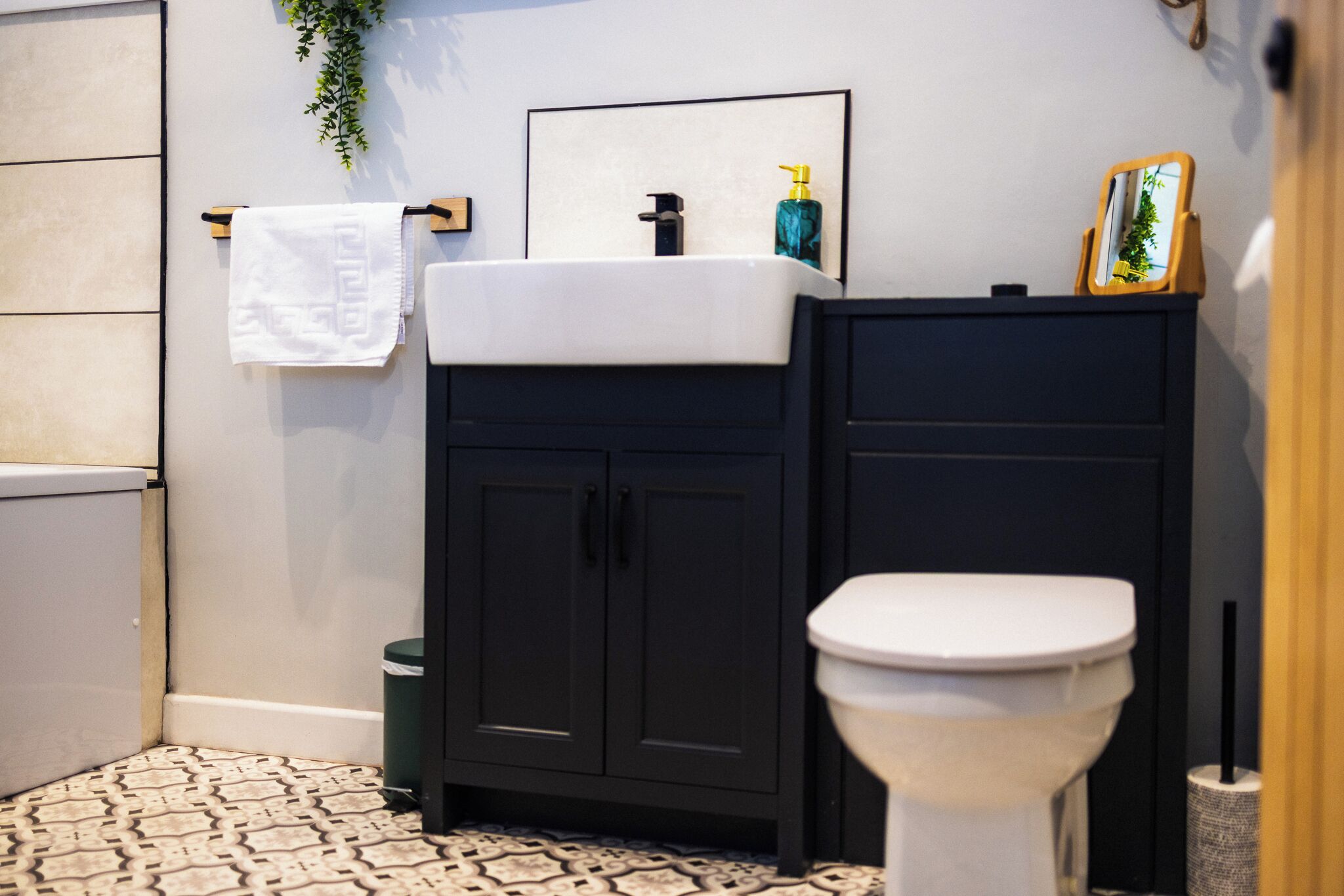 Un baño con inodoro blanco, armarios negros, lavamanos blanco y espejo.