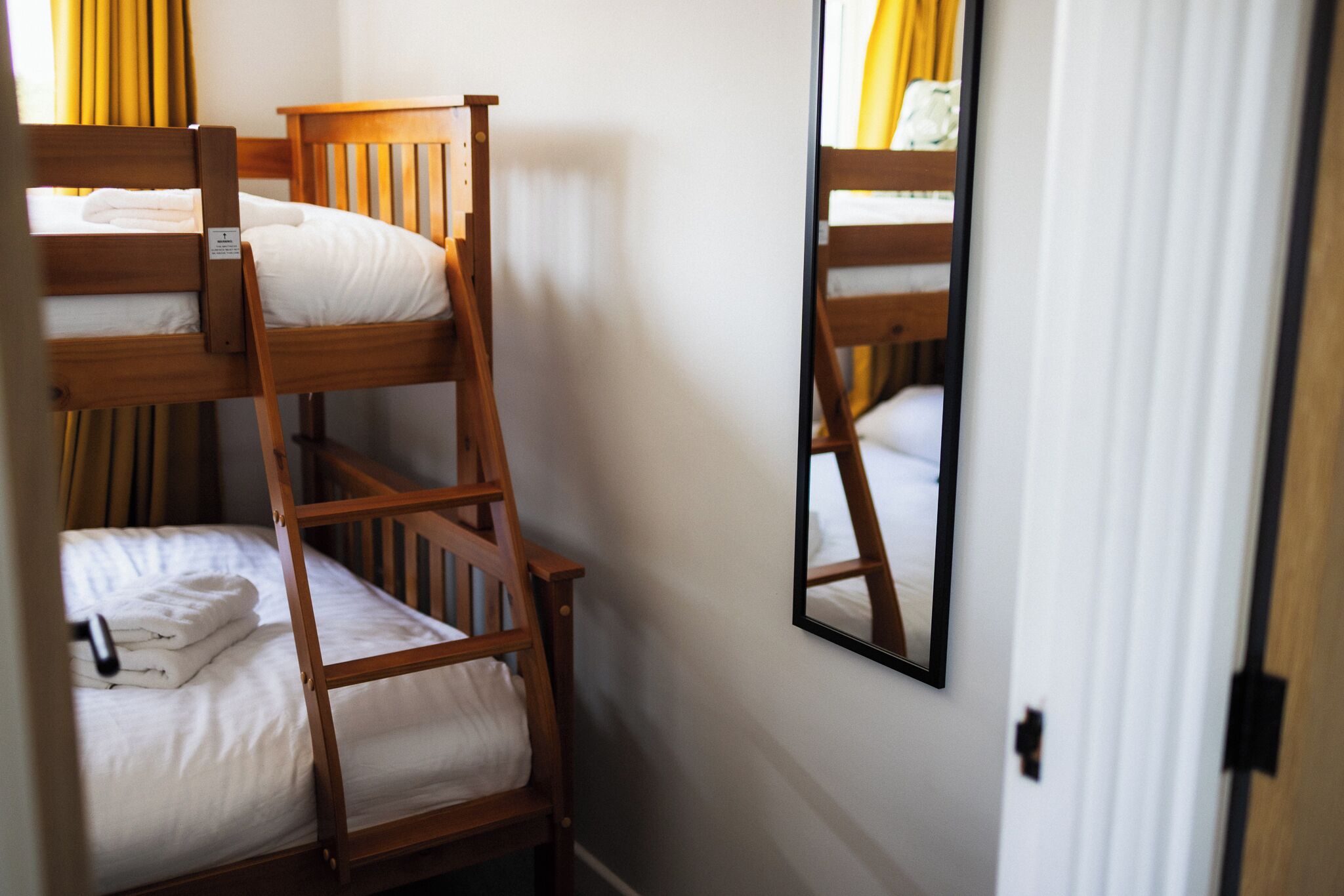 A bunk bed room with a wooden ladder and a mirror on the wall.