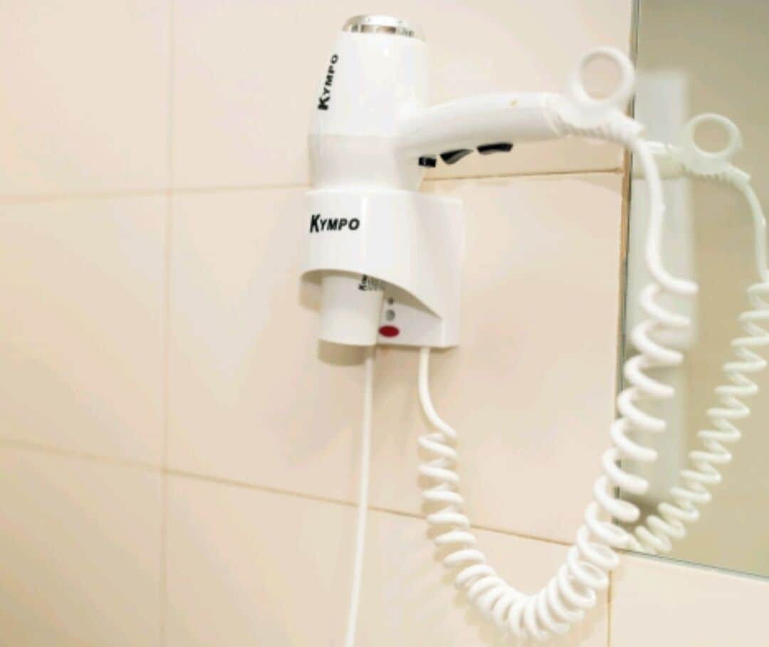 A white hairdryer with a cord plugged into a wall socket.