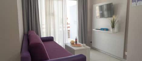 Una sala de estar moderna con un sofá púrpura, un televisor de pantalla plana montado en la pared y una mesita con aperitivos.