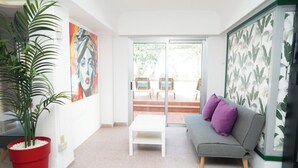 A modern living room with a grey sofa, a white coffee table, a red potted plant, and a large painting on the wall. - Las Gacelas Playa del Ingles (San Bartolome de Tirajana)