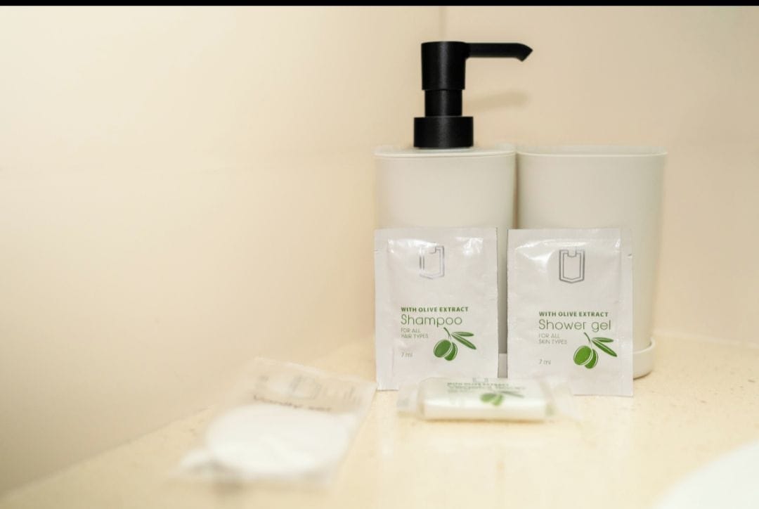 A bathroom with a pump dispenser, two bottles of shampoo and shower gel, and a bar of soap.
