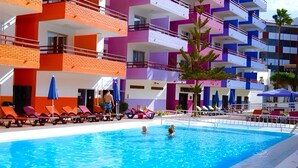 A swimming pool with sun loungers and a multi-story building with balconies in the background. - Las Gacelas Playa del Ingles (San Bartolome de Tirajana)