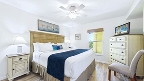 A bedroom with a bed, nightstands, a dresser, a chair, a ceiling fan, and artwork on the walls.
