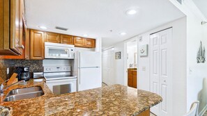 A kitchen with granite countertops, wooden cabinets, a built-in microwave, oven, and refrigerator.